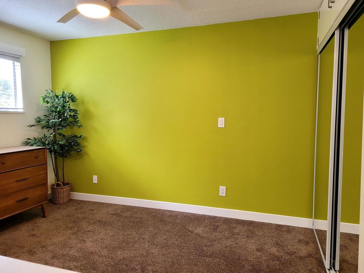 Residential bedroom painted by Davor's Painting with an olive green accent wall, white ceiling, brown carpet, and a mid-century walnut dresser in the corner.